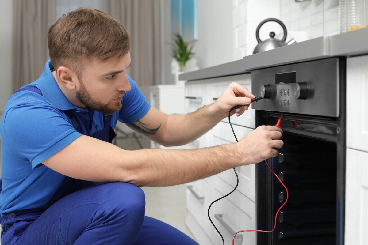 Technician testing an oven's controls with a multimeter during a repair