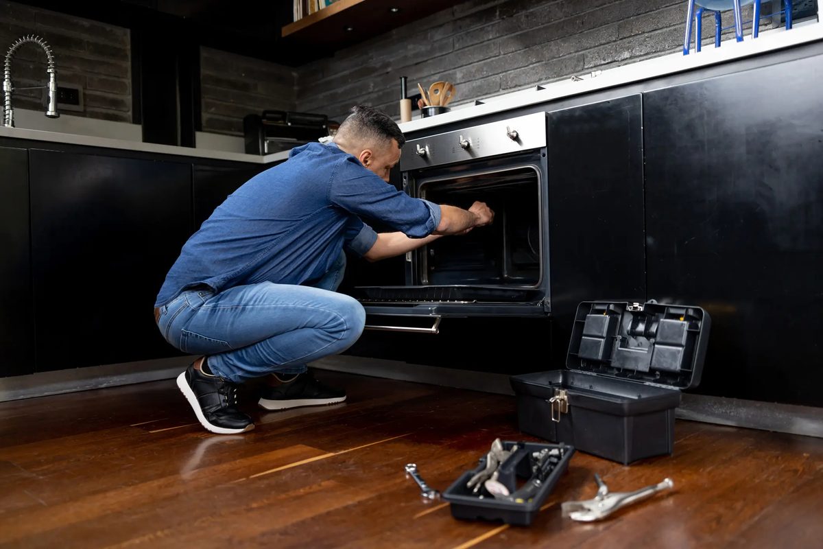 Appliance technician's open toolbox and hand tools beside a built-in oven during a service call