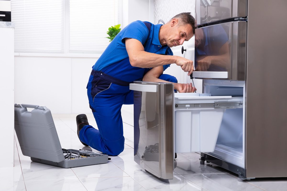 Technician repairing a stainless steel refrigerator with the freezer drawer open